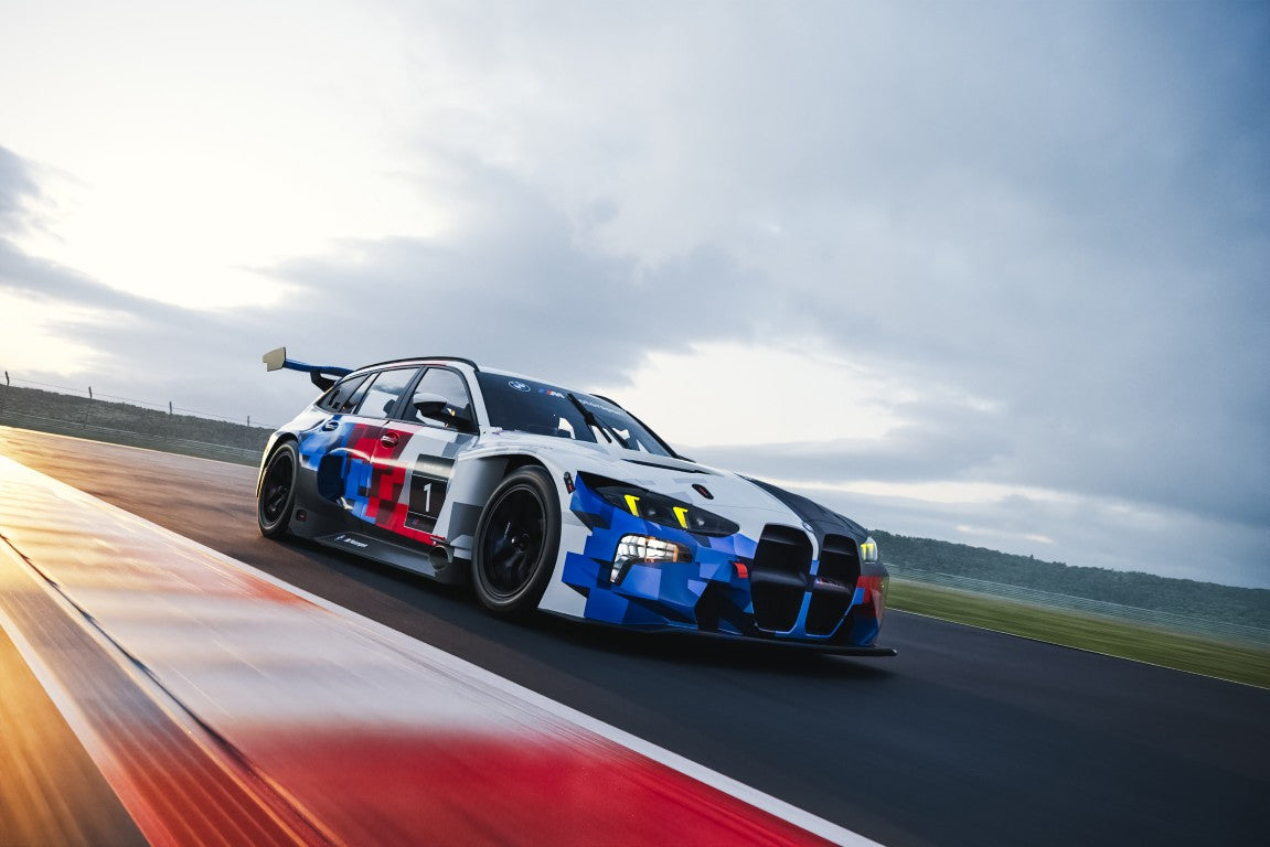 MINICHAMPS 1:64 BMW M3 Touring 24H April Fools Day Inception Design 2025 diecast model car featuring BMW M Motorsport camouflage livery, front left three-quarter view with detailed aerodynamic body kit, racing wheels and high-performance touring race car styling.