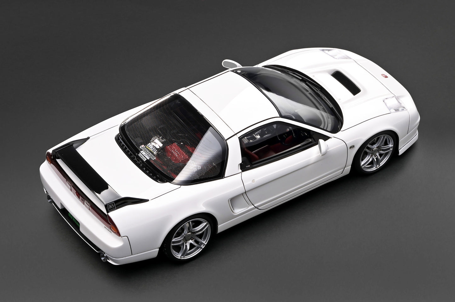 A white diecast model of a sports car, shown from a high-angle perspective on a dark gray background.