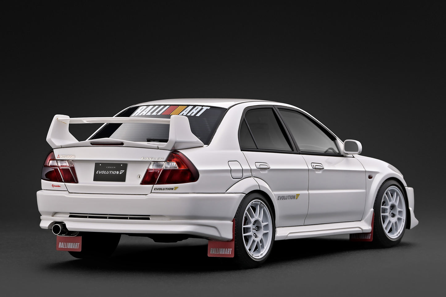 A white Mitsubishi Lancer Evolution VII race car with a large rear wing, wide body kit, and racing decals, photographed on a dark studio background.