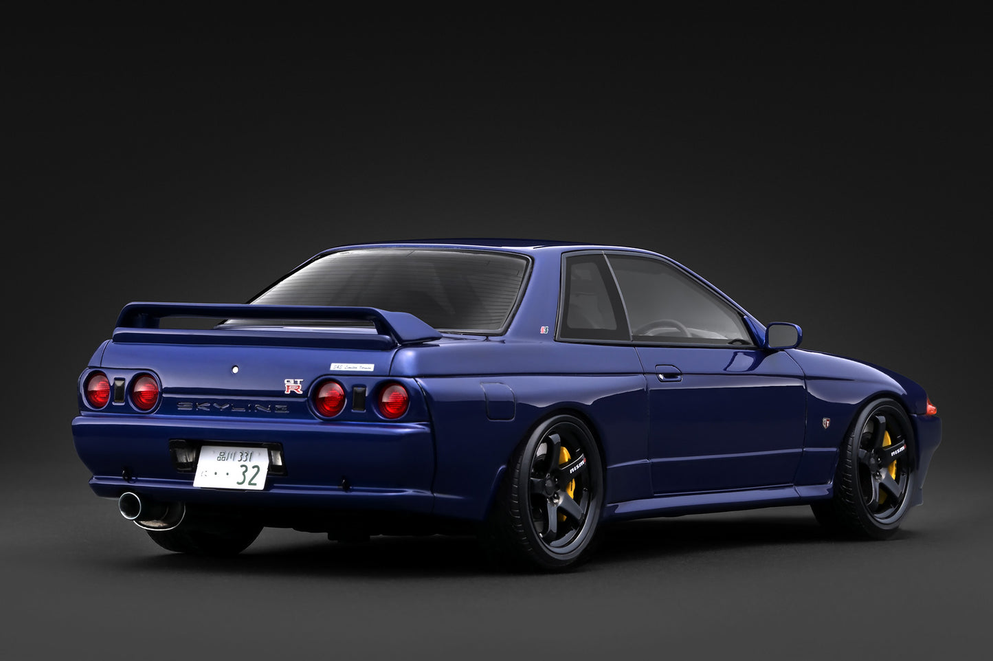 A dark blue Nissan Skyline R33 GT sports car shown from a rear three-quarter angle against a dark gray studio background.