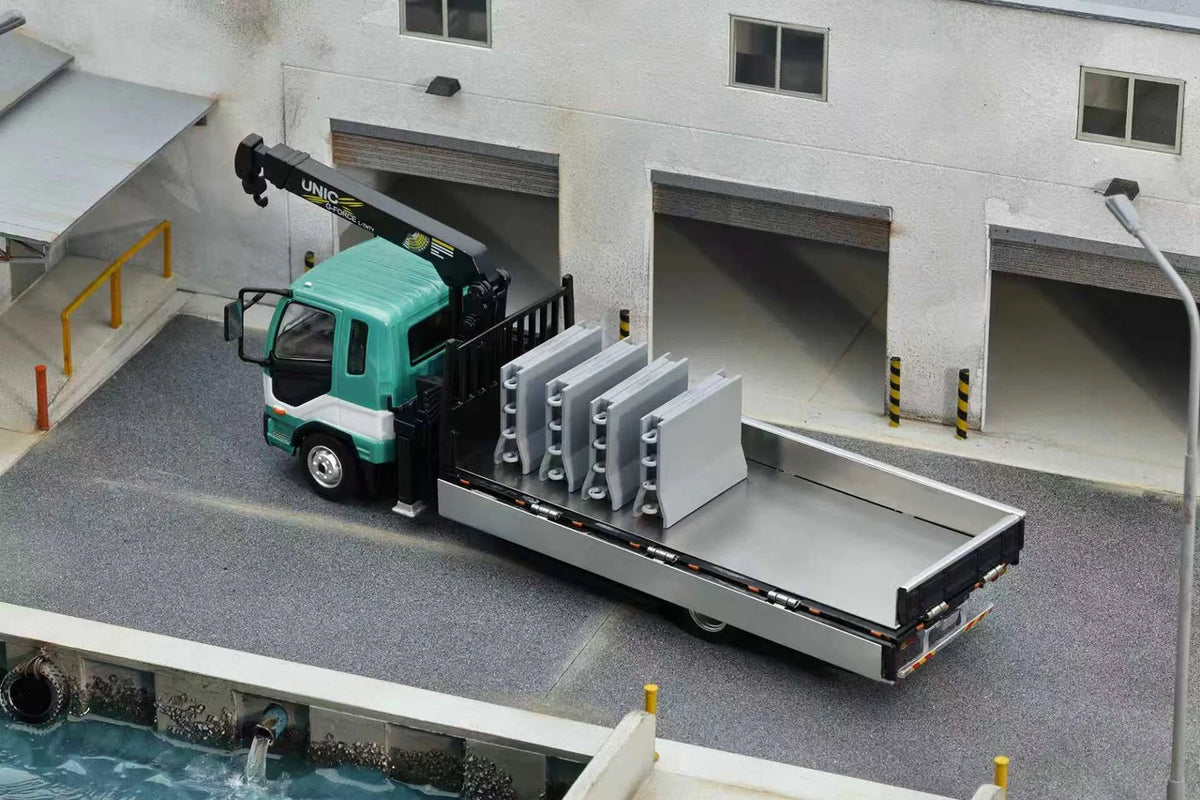 GCD 1:64 Mitsubishi Fuso Fighter (1024) Flatbed Truck with UNIC Crane Green and White No.633 KS-082-633 diecast model, featuring a turquoise green and white cab, black UNIC hydraulic crane with hook, silver flatbed with lowered side panels, four removable grey cargo barriers loaded upright, and detailed industrial warehouse loading dock diorama.