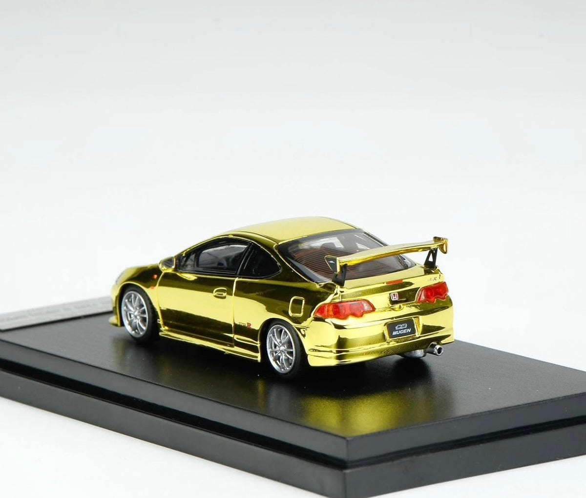 A metallic gold die-cast model of a Honda Acura Integra coupe with a rear spoiler, displayed on a black base against a white background.