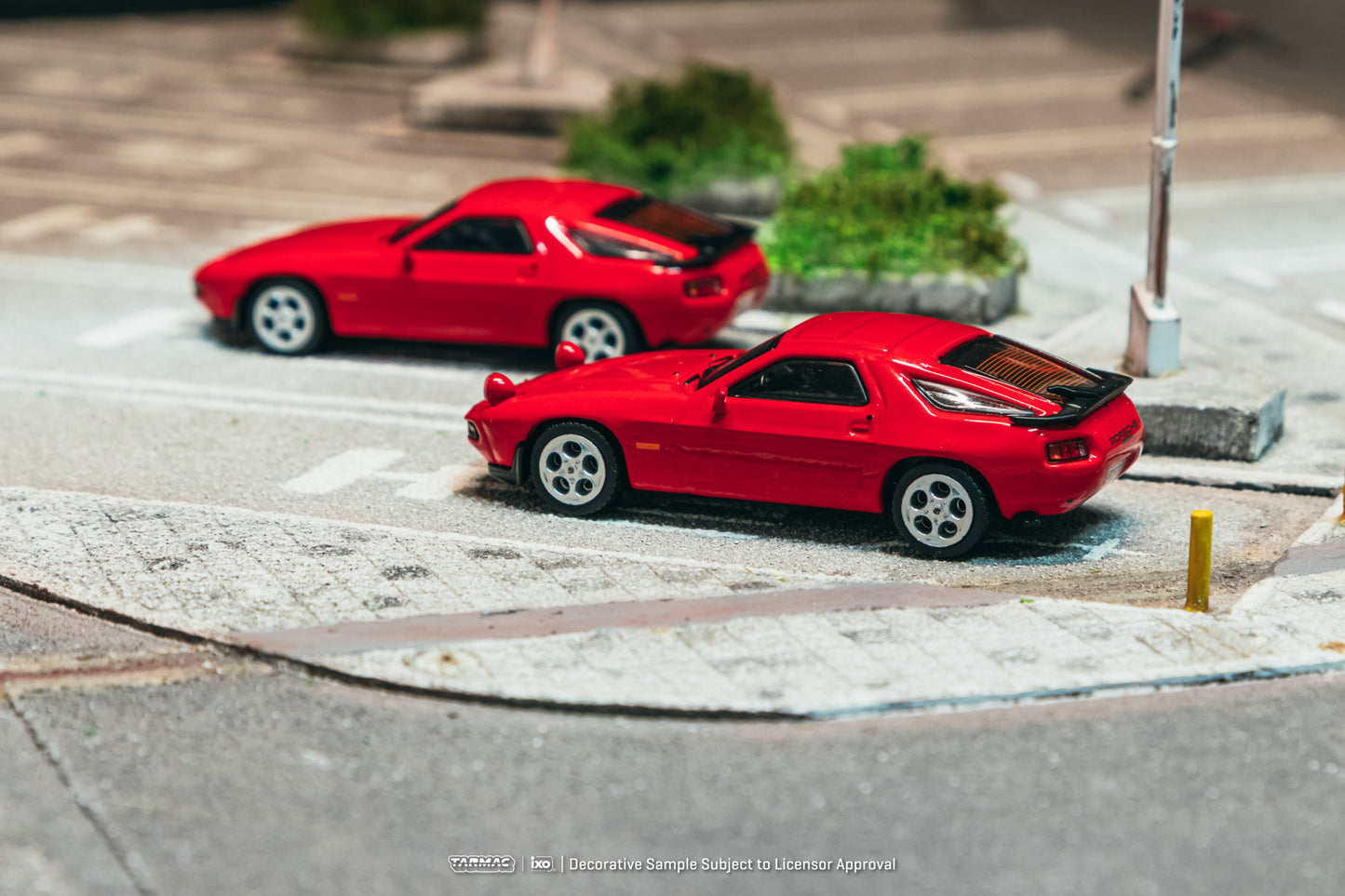 Two red toy cars on a miniature road with a blurred background