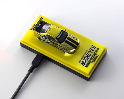 A yellow rectangular display block featuring a small metallic yellow race car model and bold black text reading 'MOONEYES' and 'MACKENZIE DRIFT CAR 96-97', shown on a white background with a black cable plugged in.