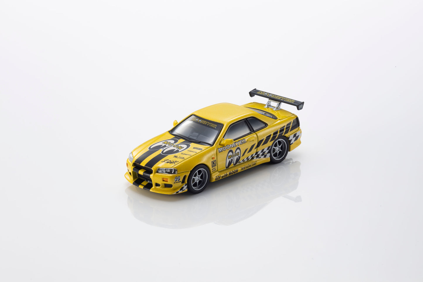 A yellow die-cast model sports car with black racing stripes, decals, and a rear spoiler, photographed on a clean white background with a soft reflection underneath.