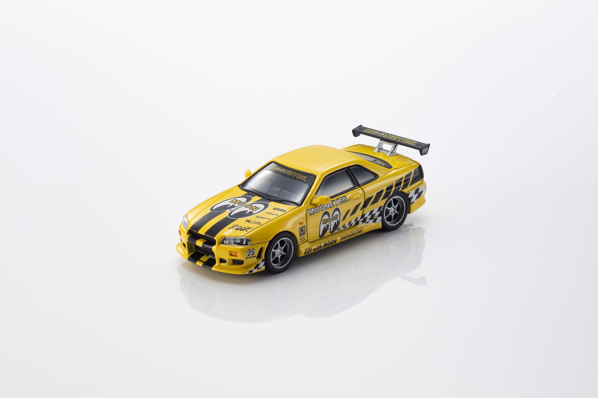 A yellow die-cast model sports car with black racing stripes, decals, and a rear spoiler, photographed on a clean white background with a soft reflection underneath.