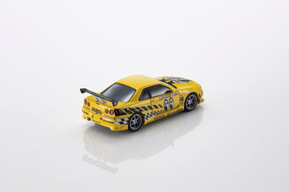 A yellow die-cast model car with black and yellow checkered graphics, a rear spoiler, and racing decals, photographed on a clean white reflective surface.