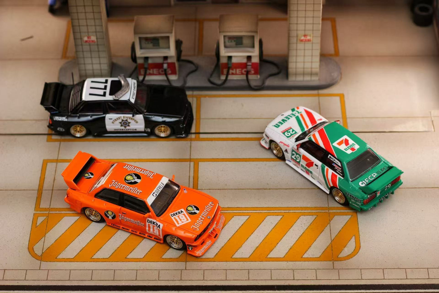 Three toy cars on a tiled floor with a gas station model in the background