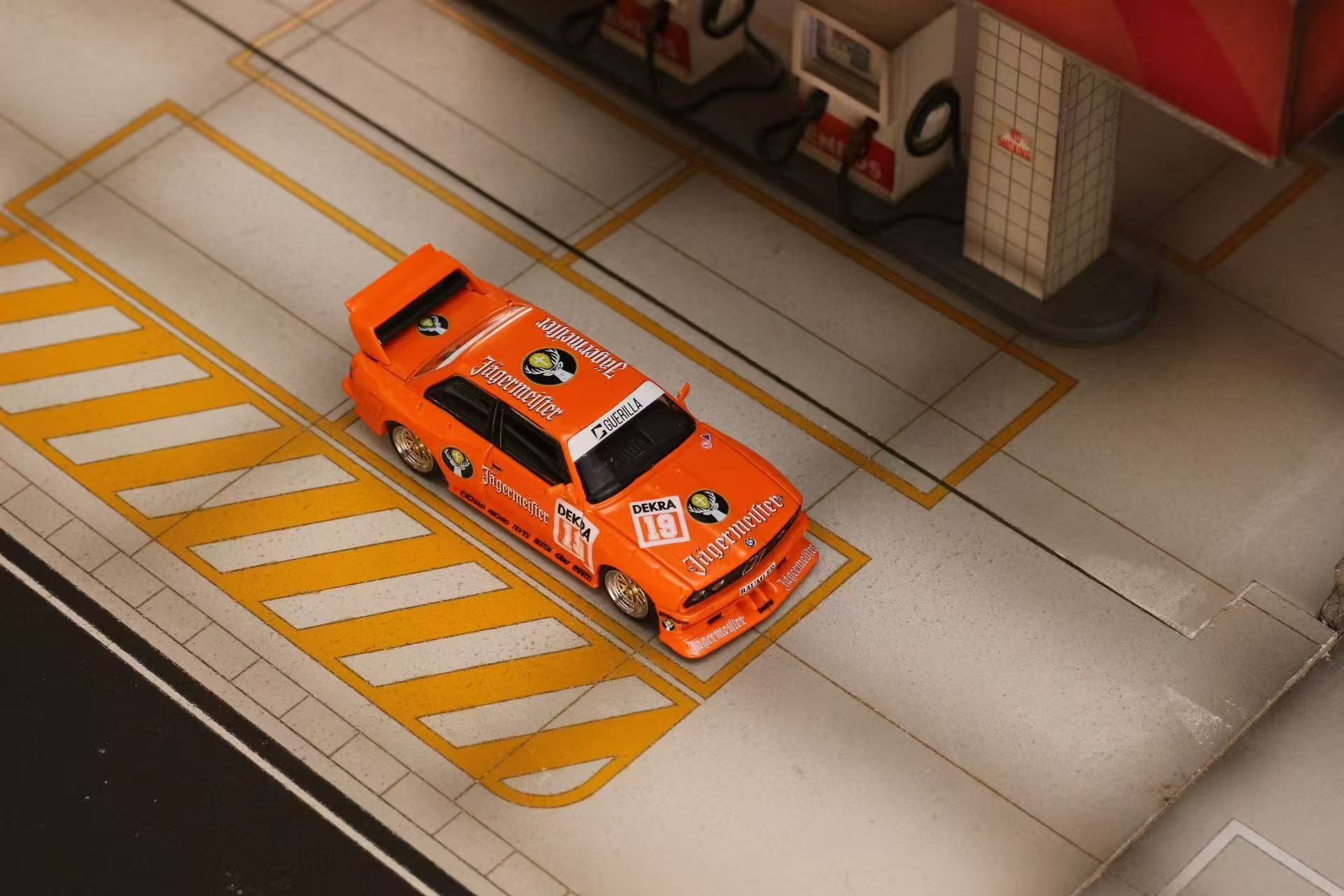 Model car on a scale model race track with a small building in the background