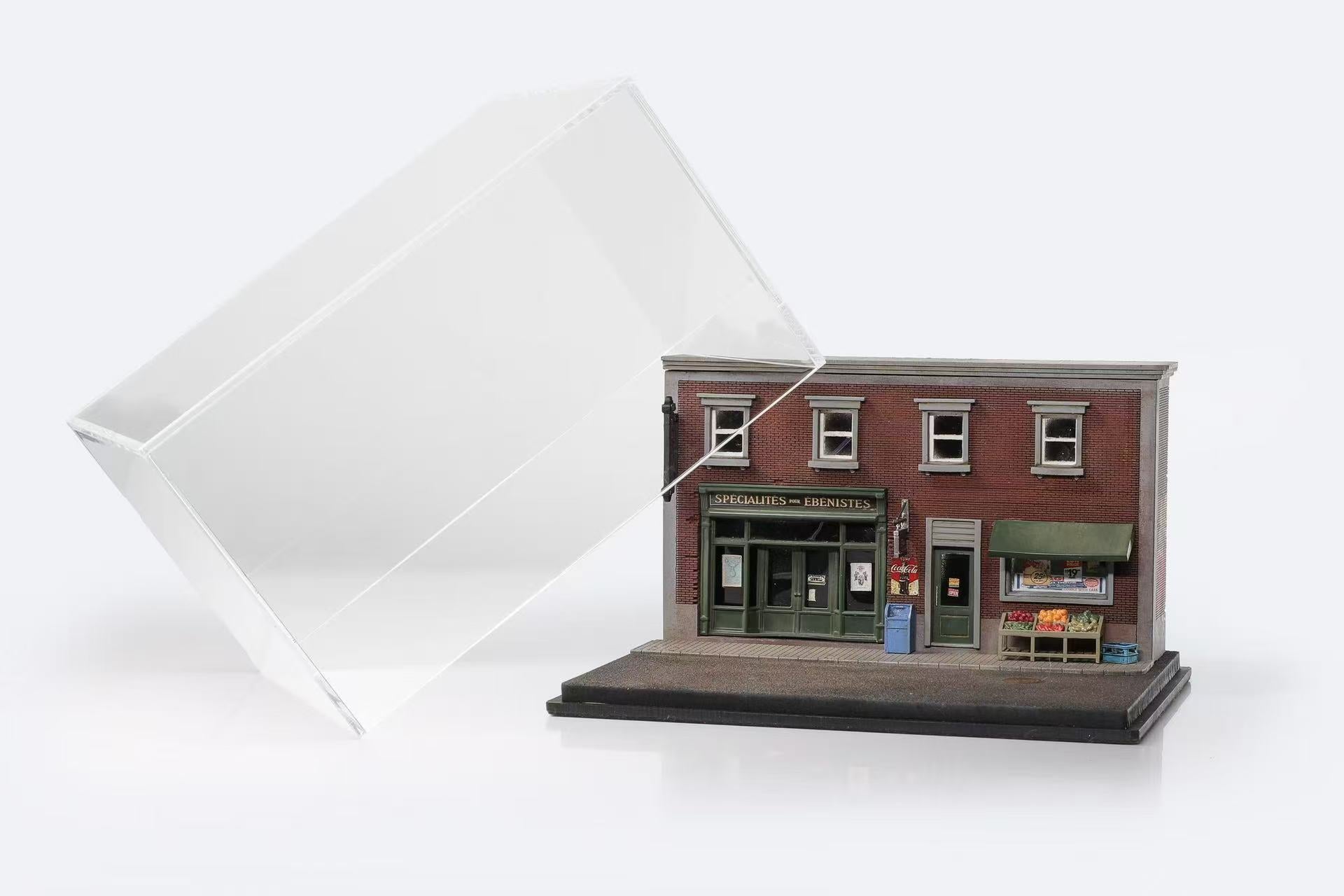 Miniature model of a red brick two-story store with green doors and awnings, featuring detailed exterior items, under a tilted clear display case.
