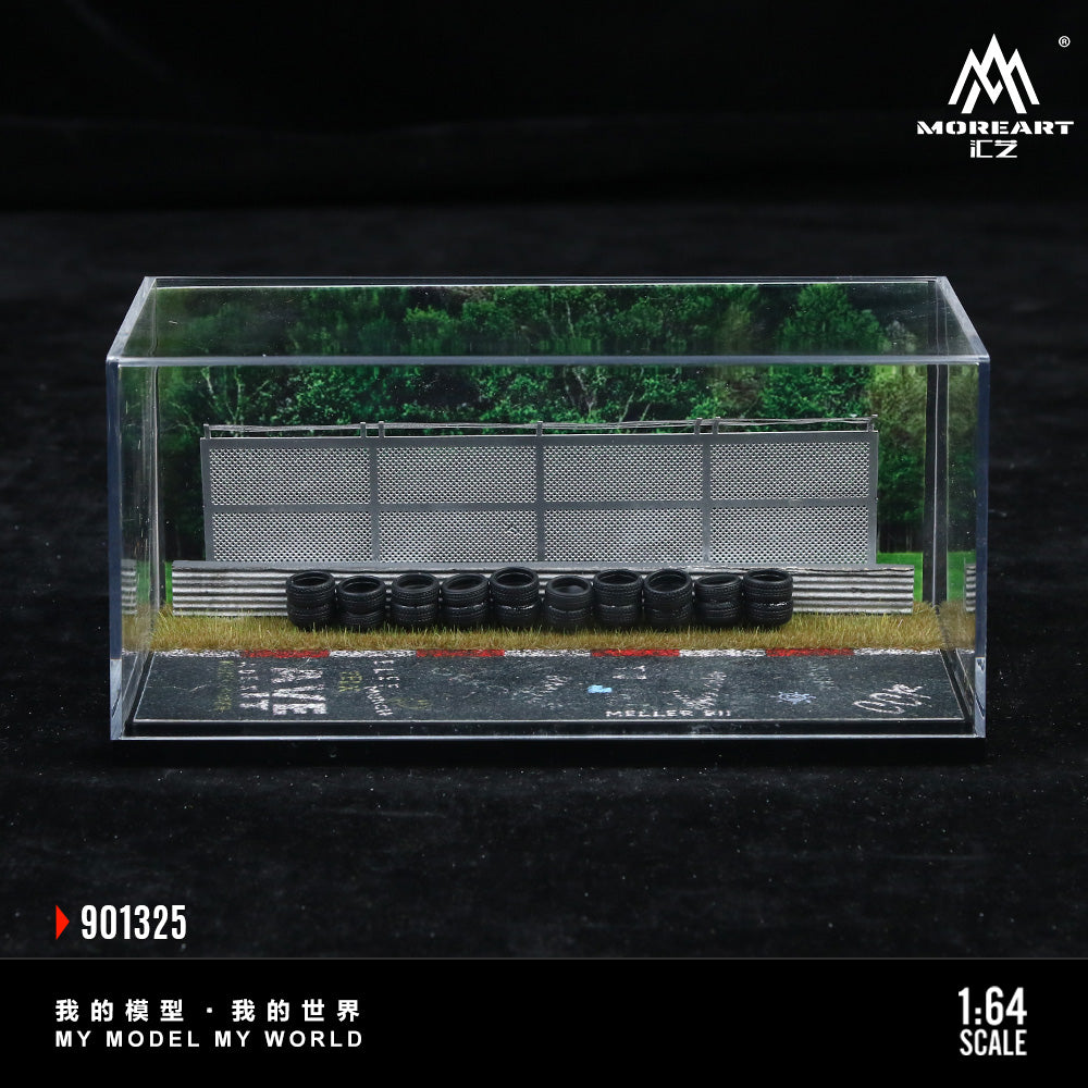 Model landscape with trees, building, and tires in a clear display case on a dark background.