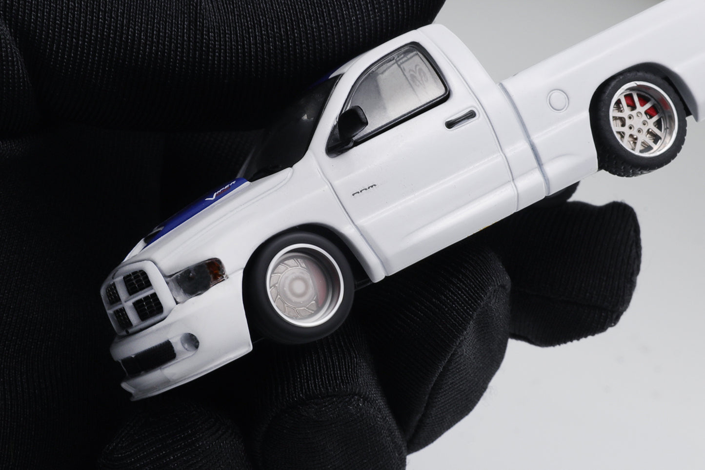 White toy truck held by a gloved hand against a neutral background