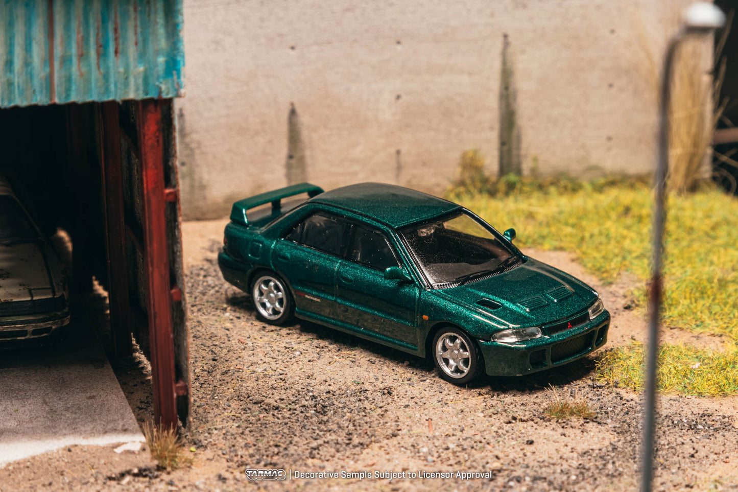 Green model car parked outdoors near a corrugated metal structure.