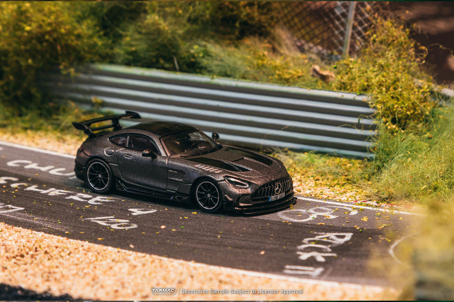 Model car on a miniature race track with greenery and a fence in the background