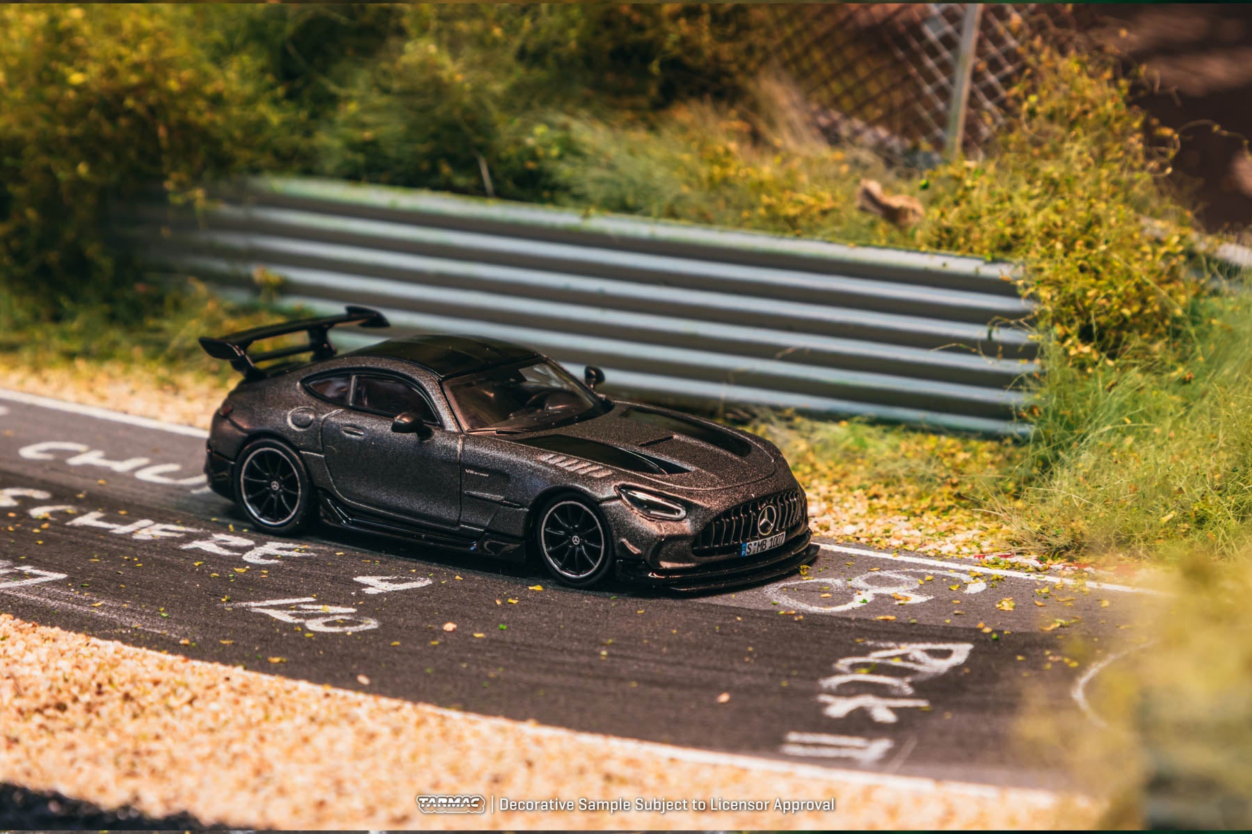 Model car on a miniature race track with greenery and a fence in the background
