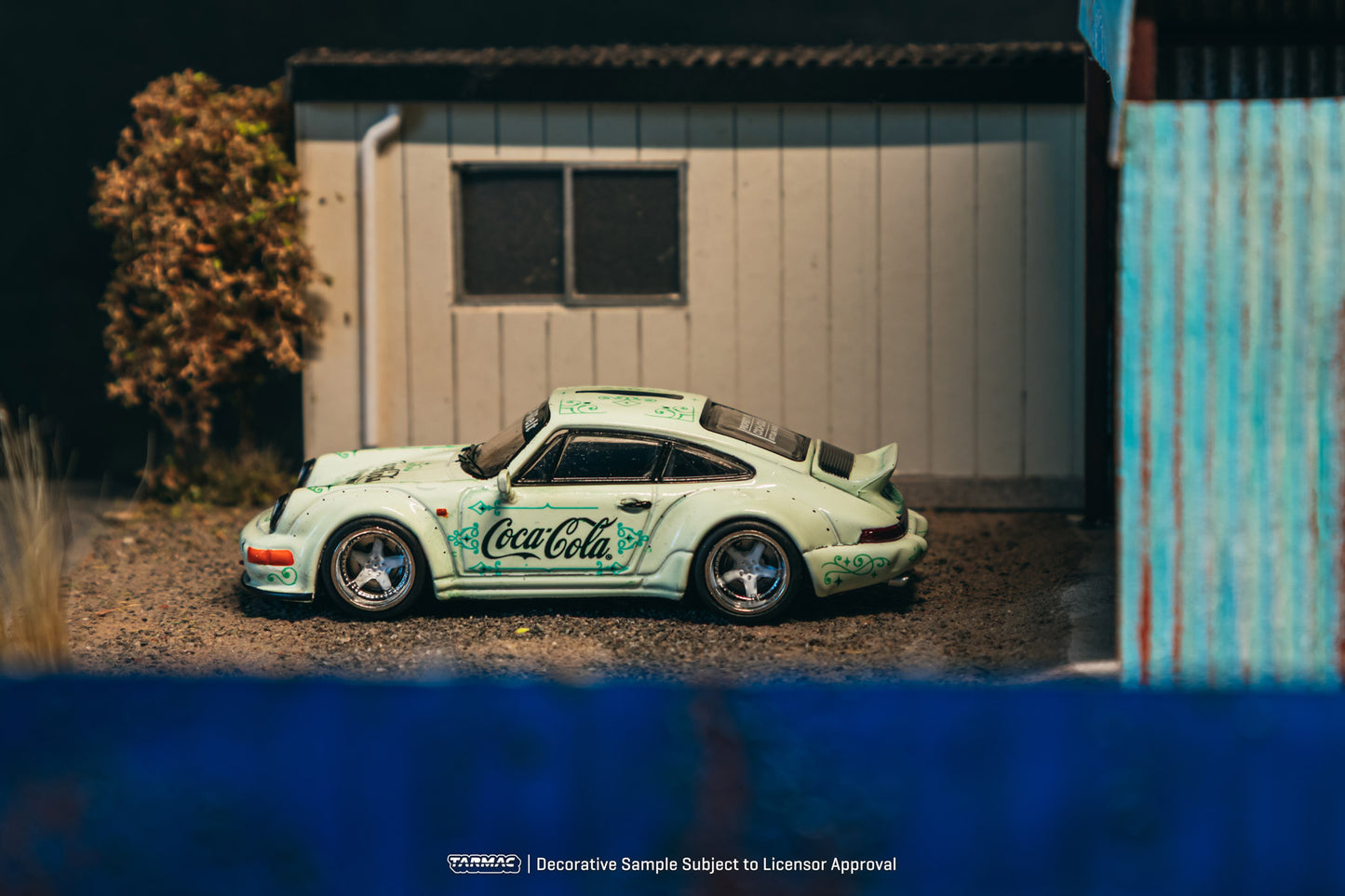 Model car with Coca-Cola branding on a gravel surface in front of a building.