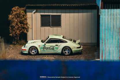 Model car with Coca-Cola branding on a gravel surface in front of a building.