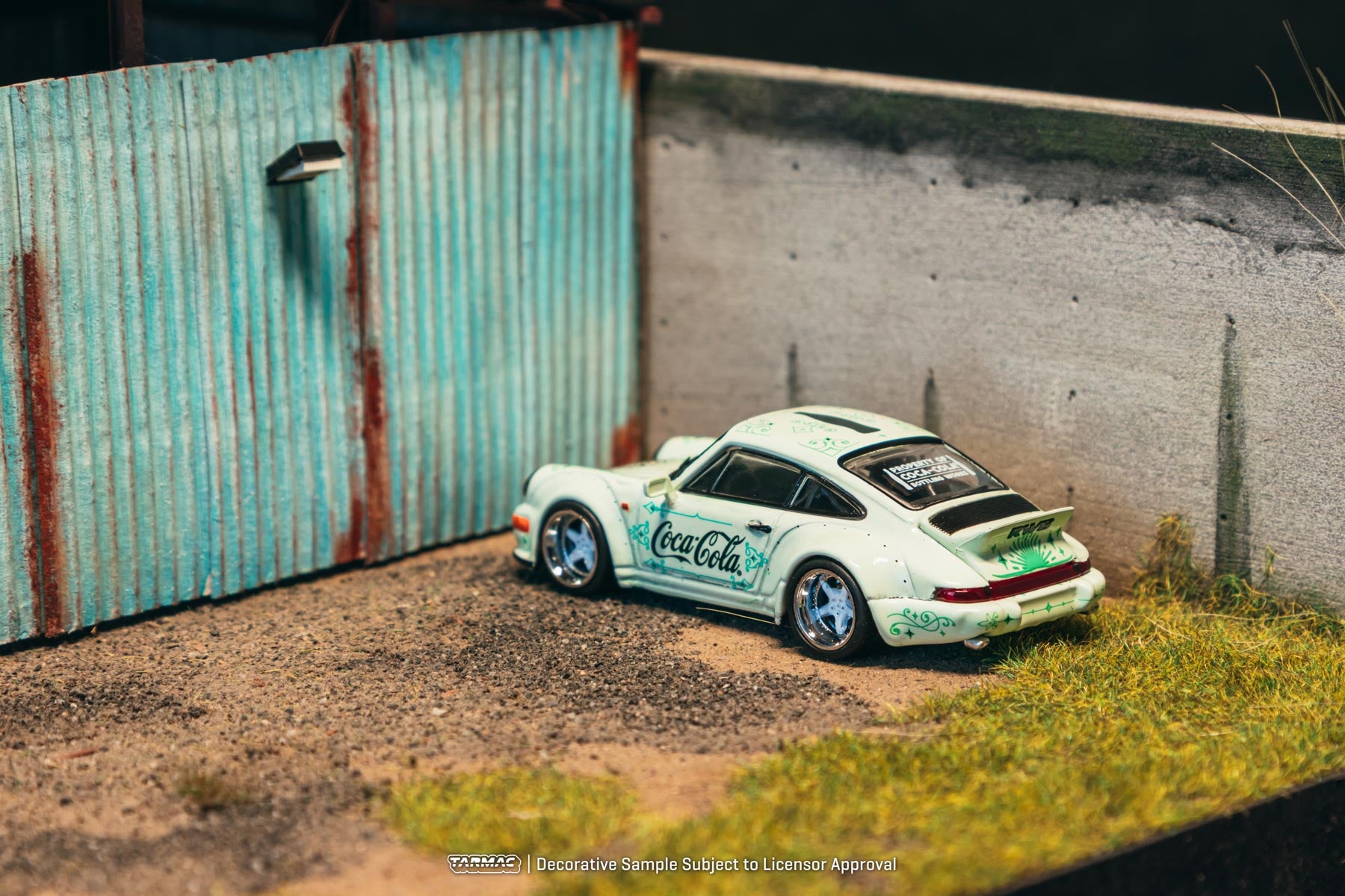Model car with Coca-Cola branding parked against a corrugated metal wall.