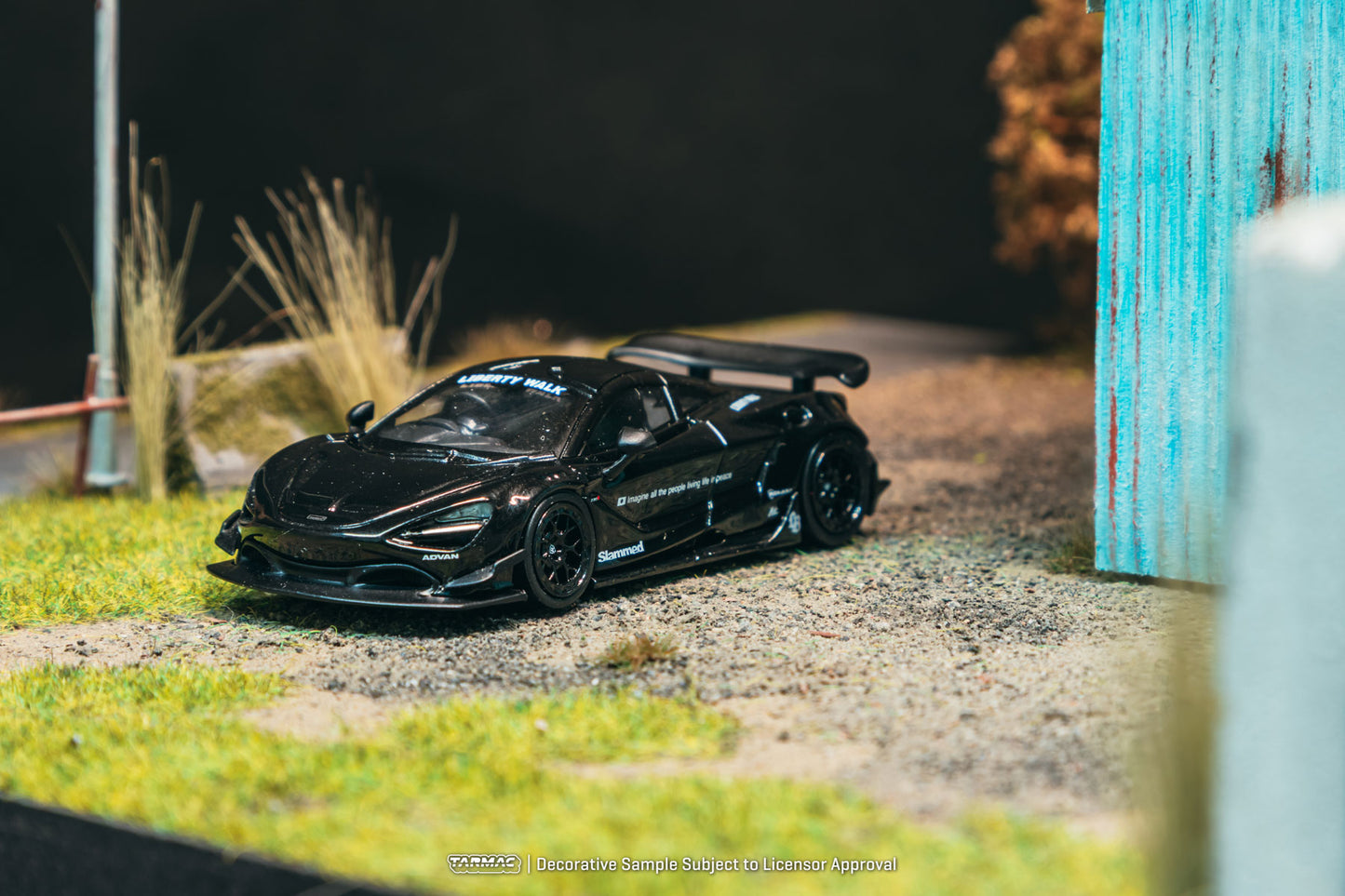 Black sports car model on a miniature road with grass and a blue wall in the background