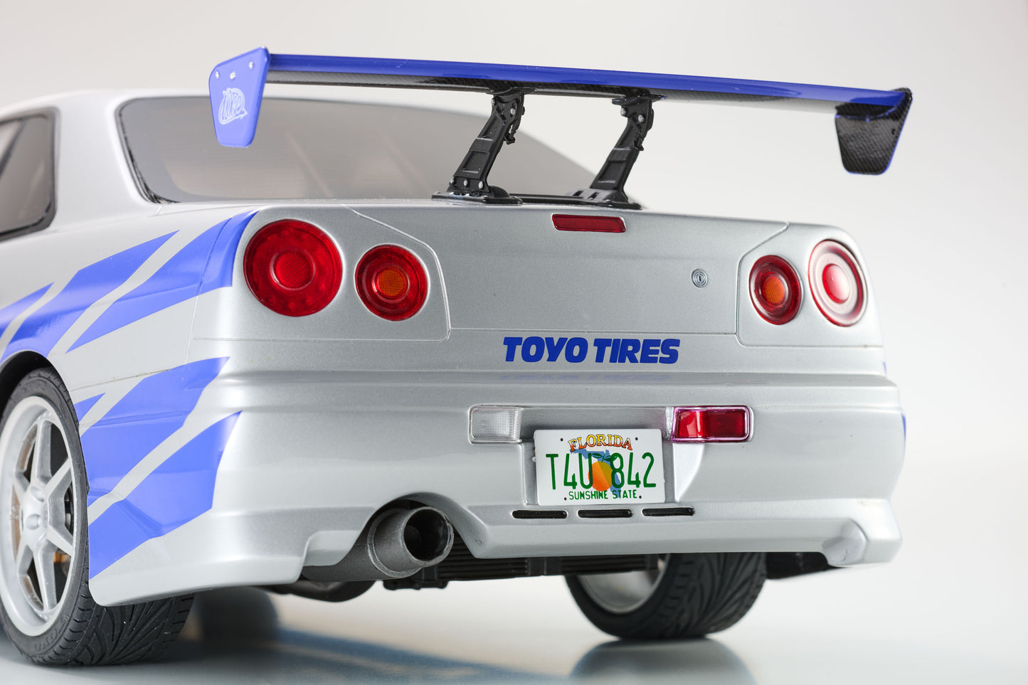 Back view of a silver car with a blue spoiler and Toyo Tires branding on a white background