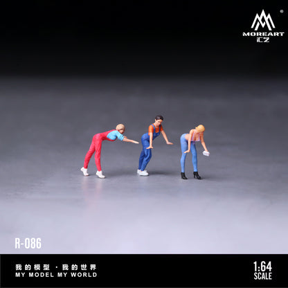 Three miniature figures in colorful outfits on a gray surface with 'MoreArt' branding.