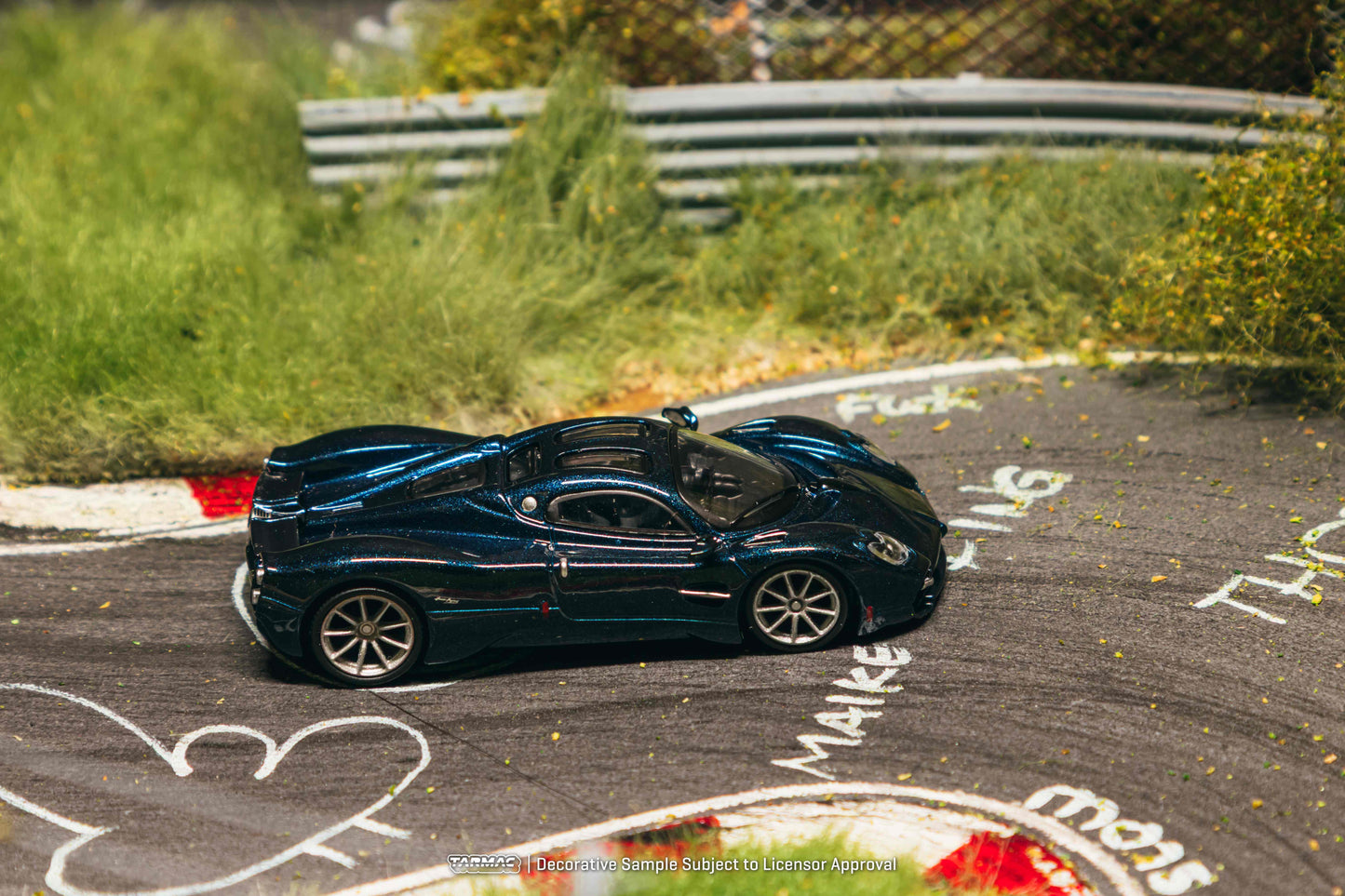Blue sports car on a race track with grass and barriers in the background