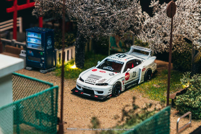 Model car on a miniature street with cherry blossom trees and a blue building in the background