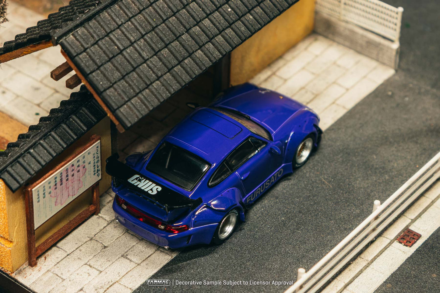Blue toy car parked in front of a small building with a tiled roof