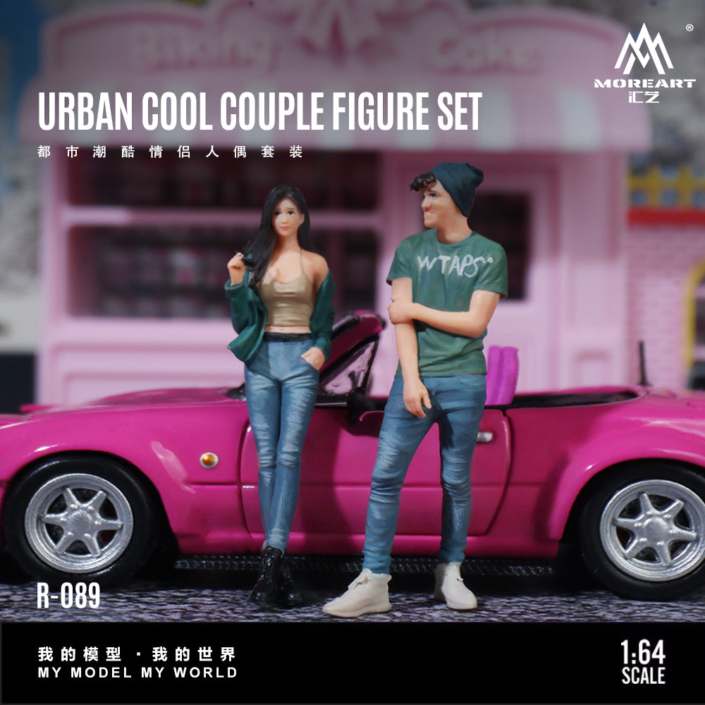Two action figures of a couple standing in front of a pink car with 'MoreArt' branding.
