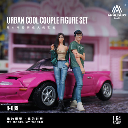 Two action figures of a couple standing in front of a pink car with 'MoreArt' branding.