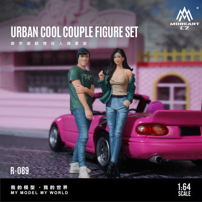 Two action figures of a couple standing in front of a pink car with 'MoreArt' branding.