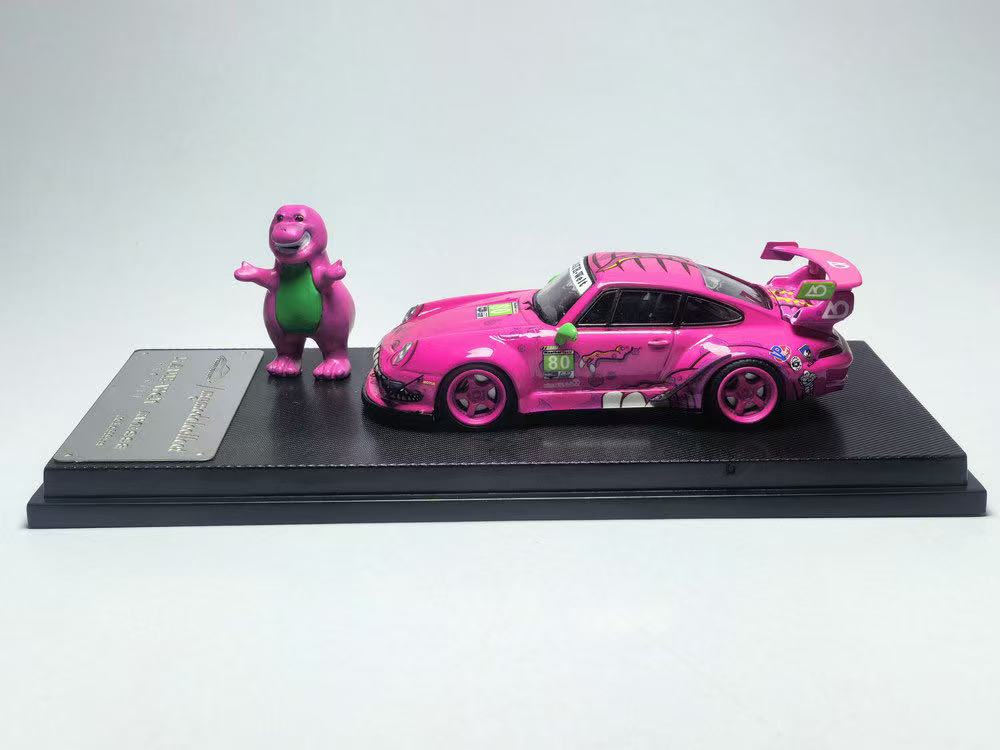 Pink toy car and Barney figure on a black platform with a white background