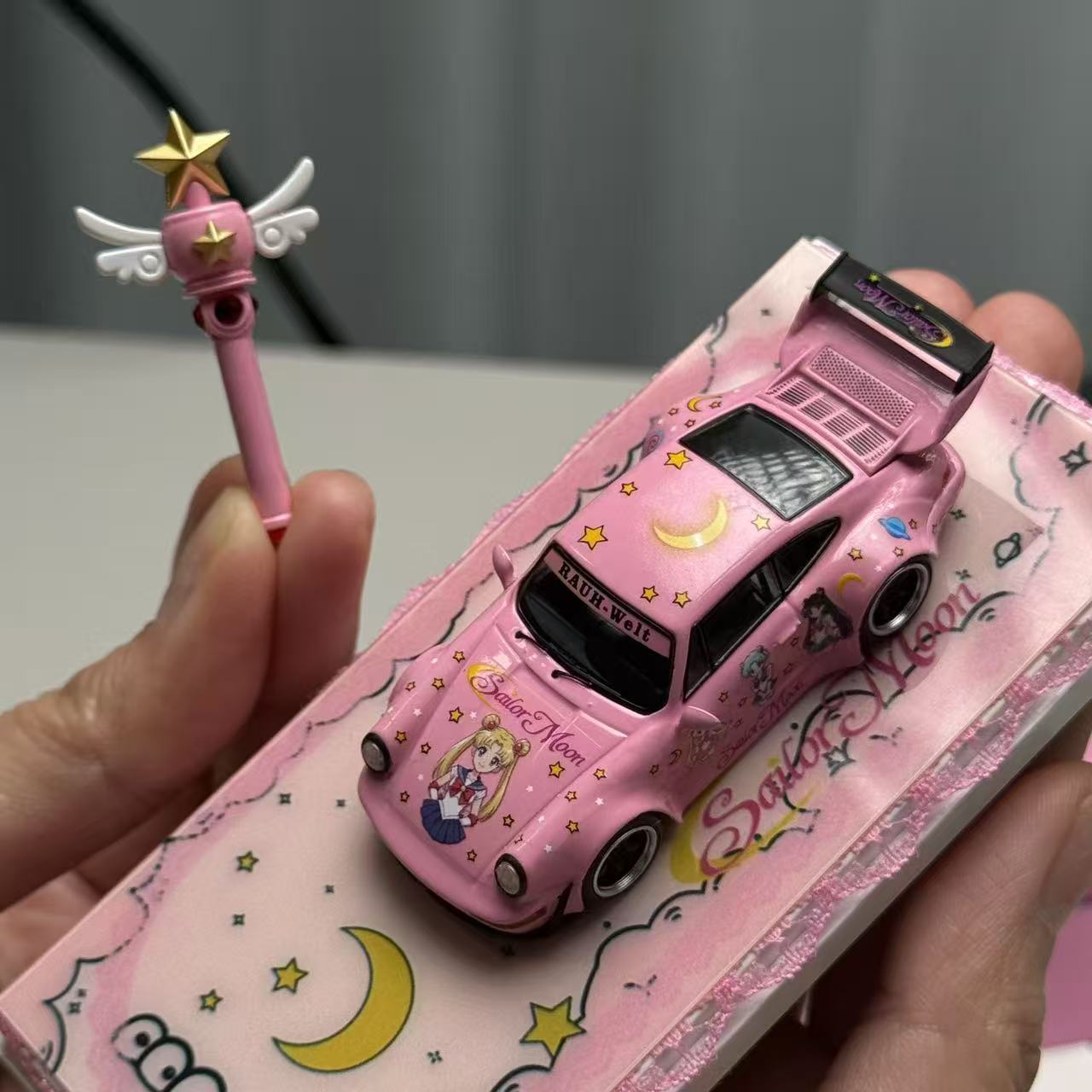 Pink toy car with cartoon design held by a hand