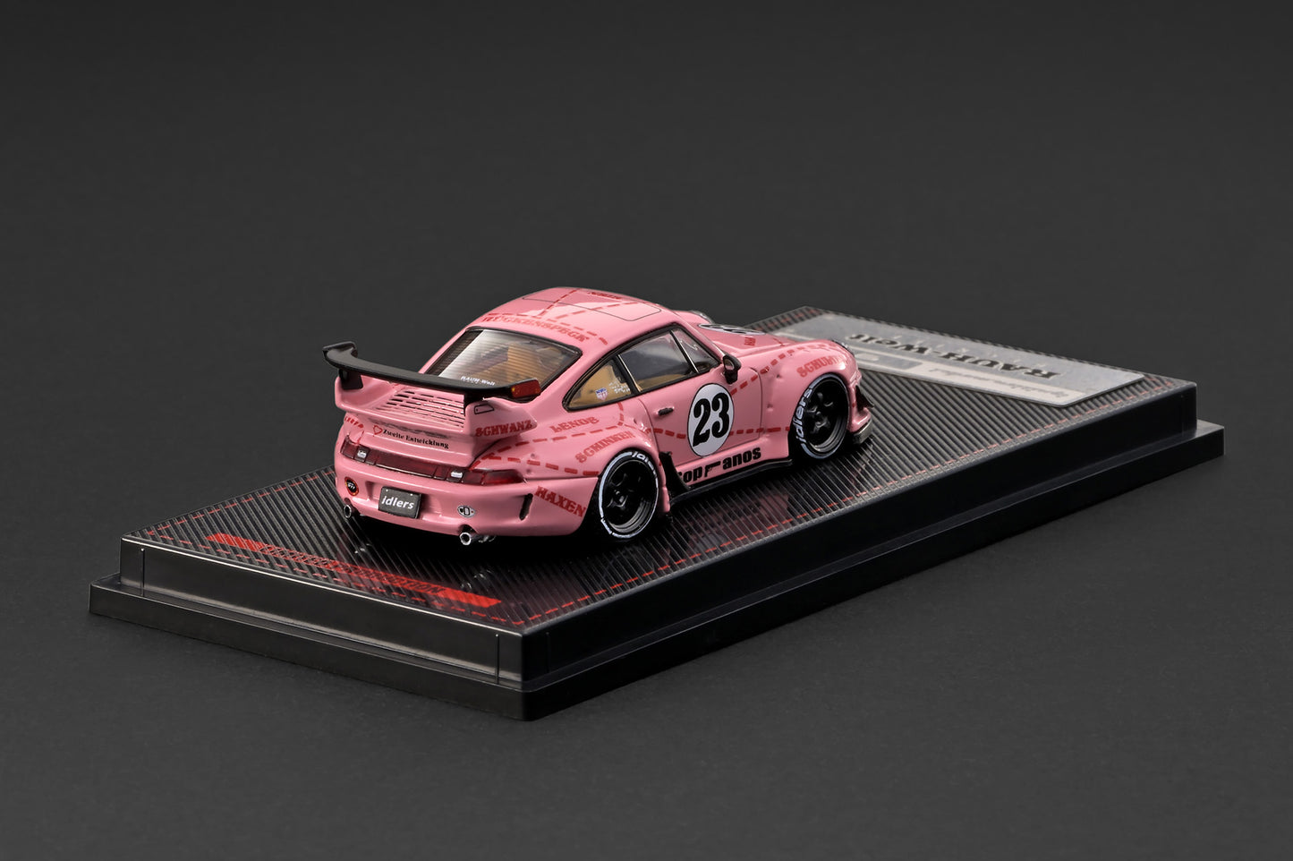 A pink Toyota Supra model car with a mottled paint pattern and number 23, displayed on a black textured base with a silver plaque.