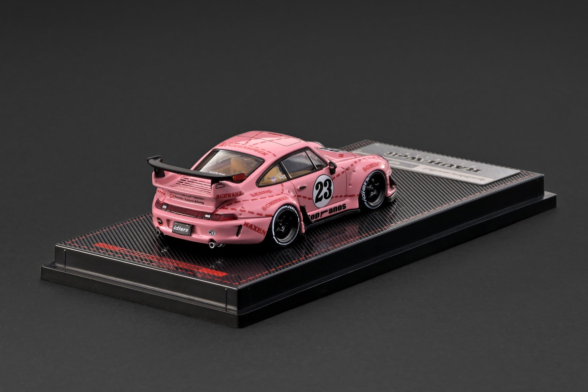 A pink Toyota Supra model car with a mottled paint pattern and number 23, displayed on a black textured base with a silver plaque.