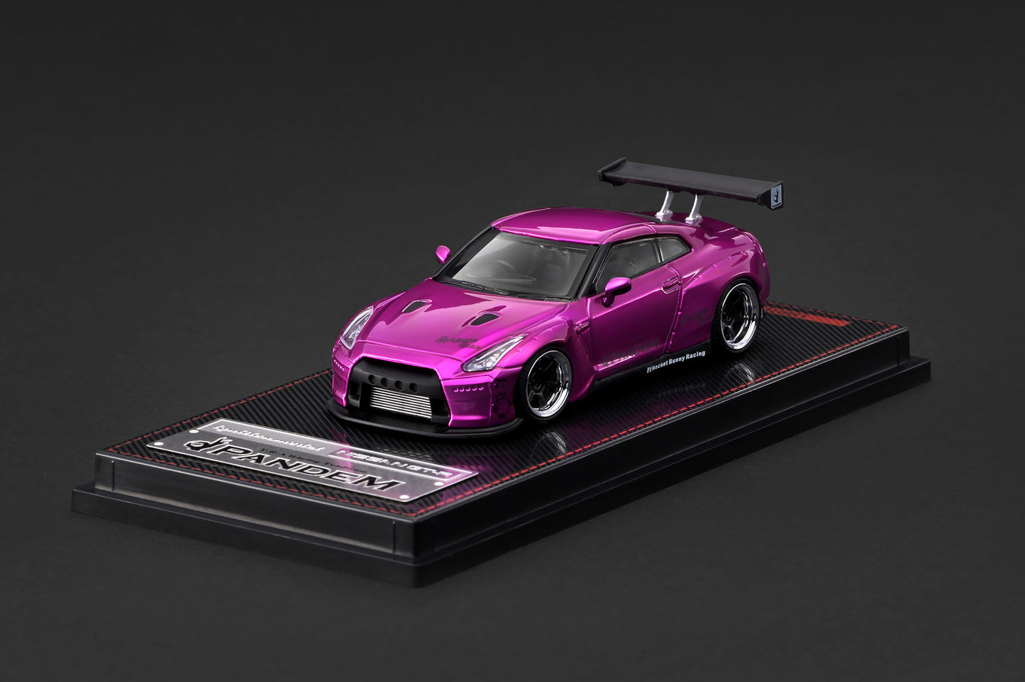 A metallic magenta-pink diecast model of a Nissan GT-R R35 sports car, displayed on a black custom base with a clear acrylic lid, set against a dark gray background.