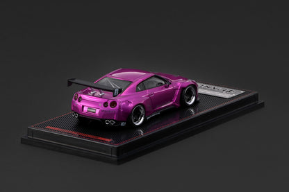 A metallic magenta-pink diecast model car with a black rear wing and black wheels, displayed on a black carbon-fiber-textured base with a silver plaque.