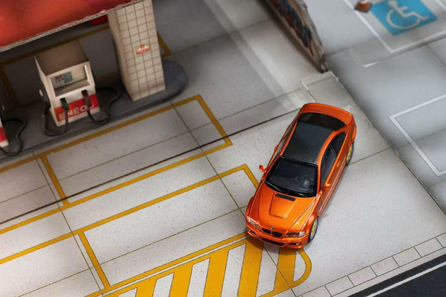 Orange car parked on a city street with a gas station and pedestrian crossing sign in the background.