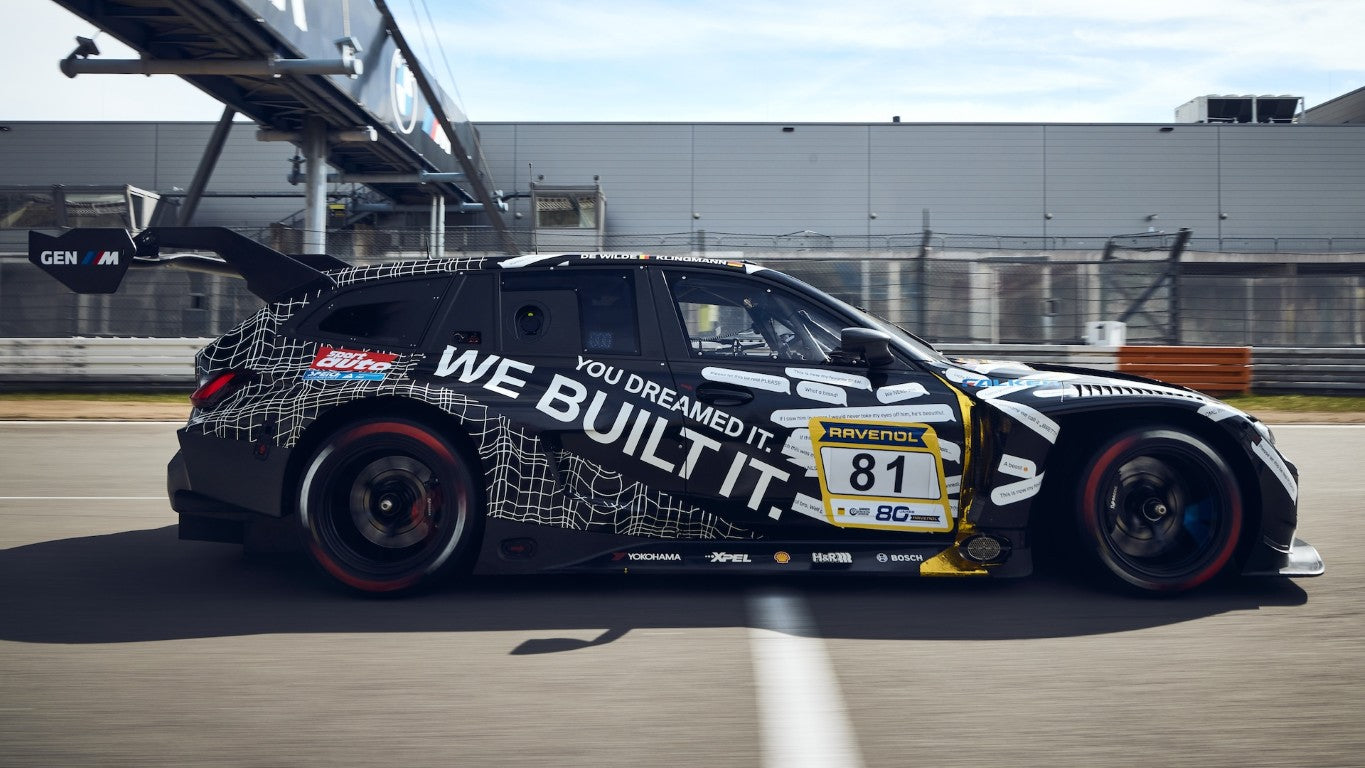 MINICHAMPS 1:64 BMW M3 Touring 24H April Fools Day Inception Design 2025 diecast model race car in BMW M Motorsport camouflage livery, left side profile view on racetrack, featuring widebody aerodynamic kit, large rear wing, racing wheels and detailed GT endurance racing design.
