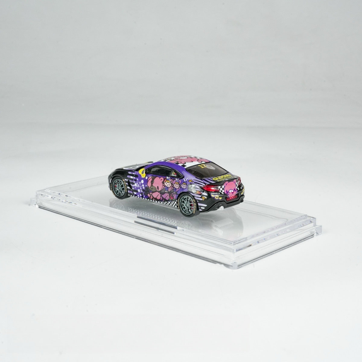 A miniature model car on a display stand, featuring vibrant cartoon graphics with a purple and black color scheme, creating a playful and cheerful vibe.