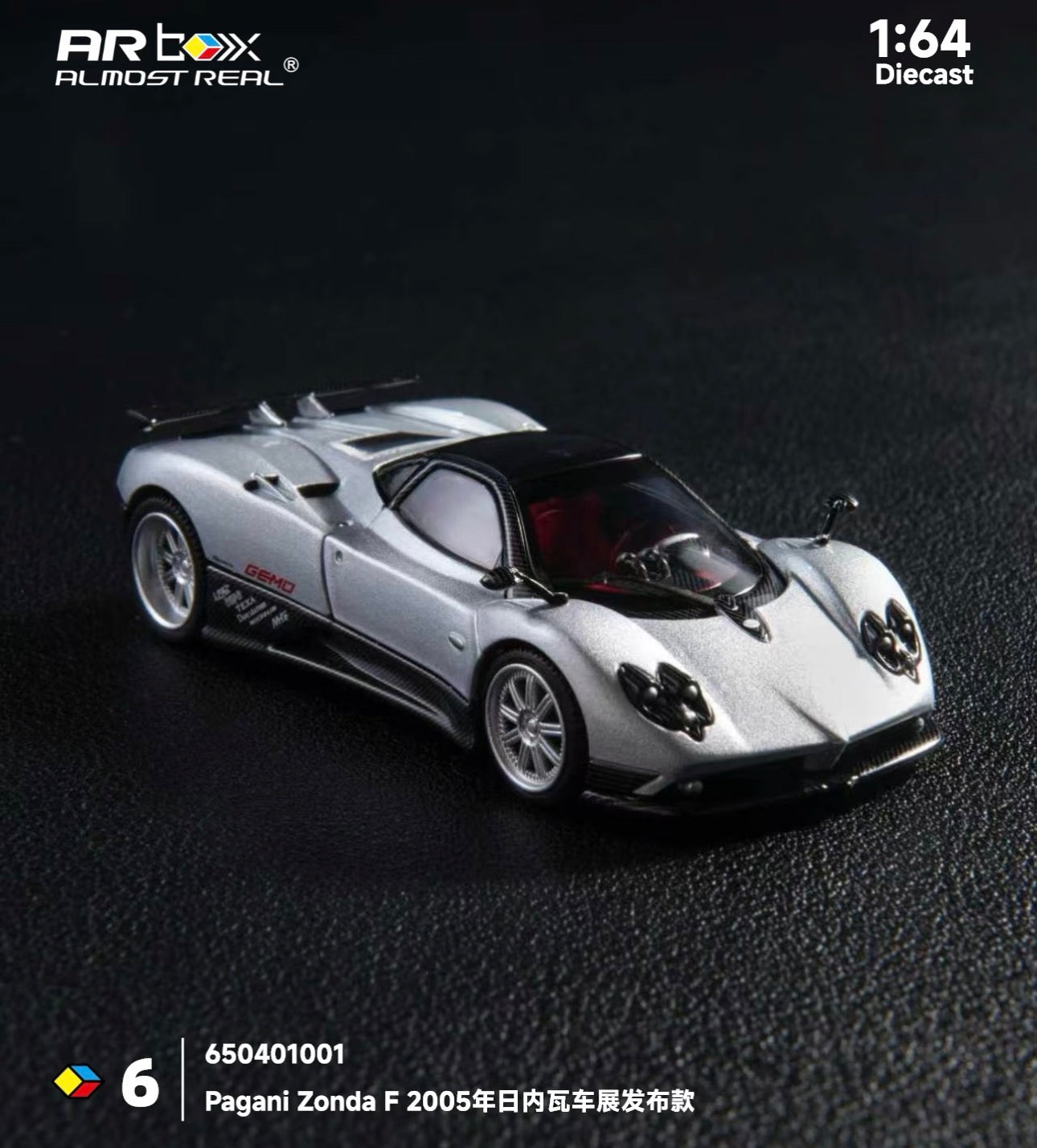 Silver Pagani Zonda F 1:64 scale diecast model on a dark textured surface. The model is detailed, showing sleek curves and a glossy finish. Text in the image includes "Pagani Zonda F 2005."