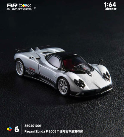 Silver Pagani Zonda F 1:64 scale diecast model on a dark textured surface. The model is detailed, showing sleek curves and a glossy finish. Text in the image includes "Pagani Zonda F 2005."