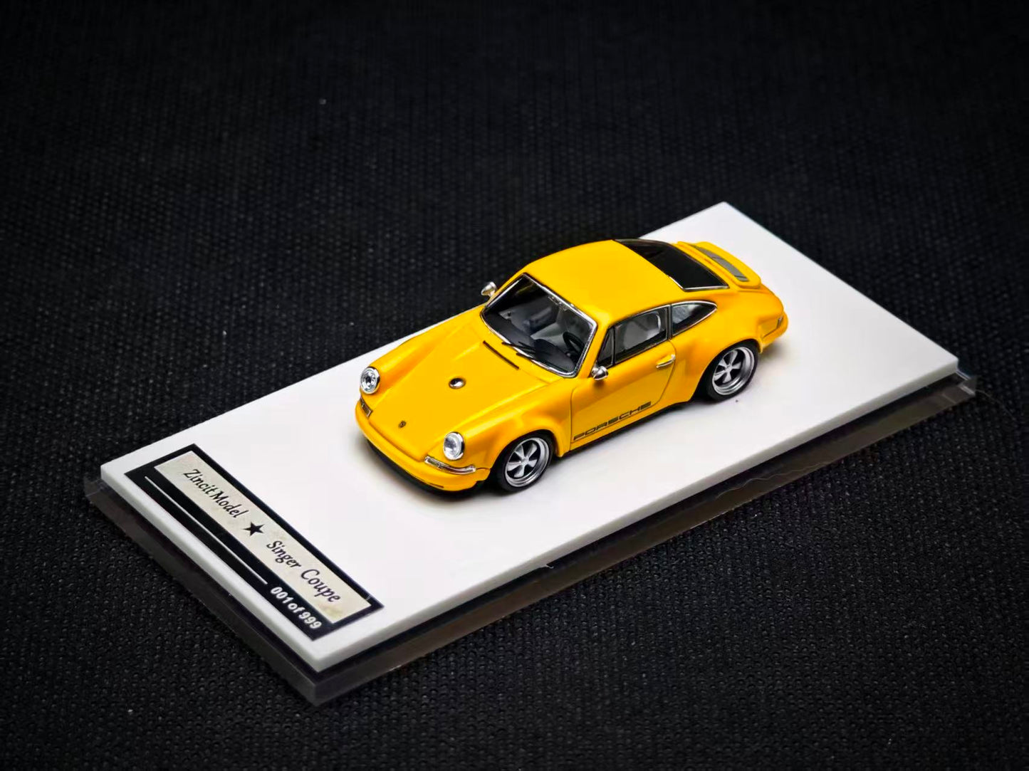 Yellow model car on a white platform with a black background
