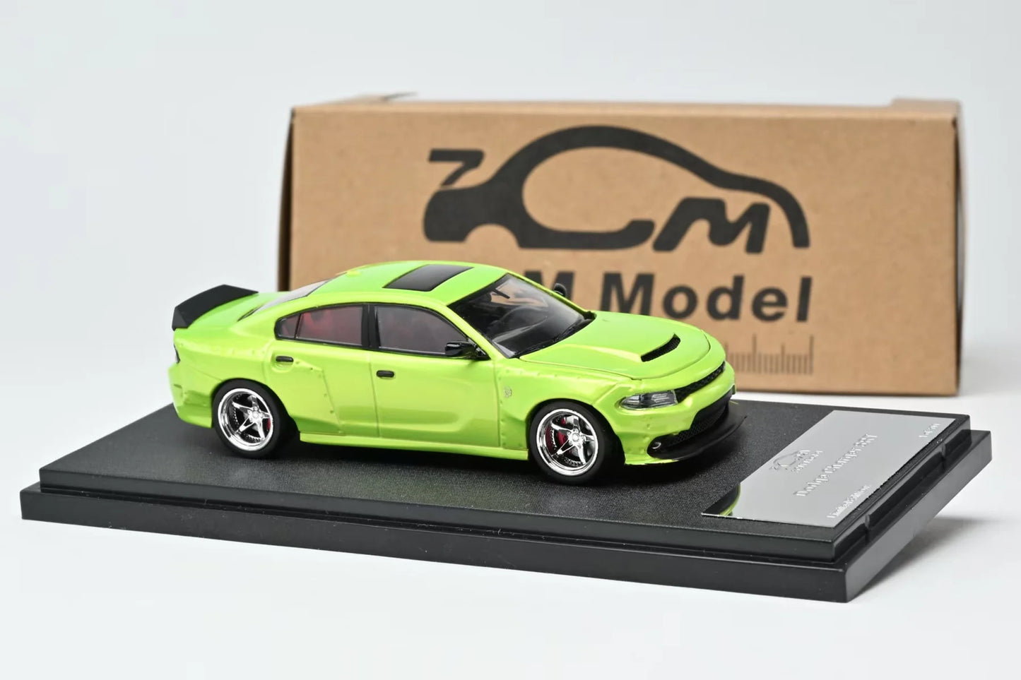 A lime green diecast model car of a Dodge Charger SRT, displayed on a black base with a silver plaque, in front of its original cardboard packaging box.