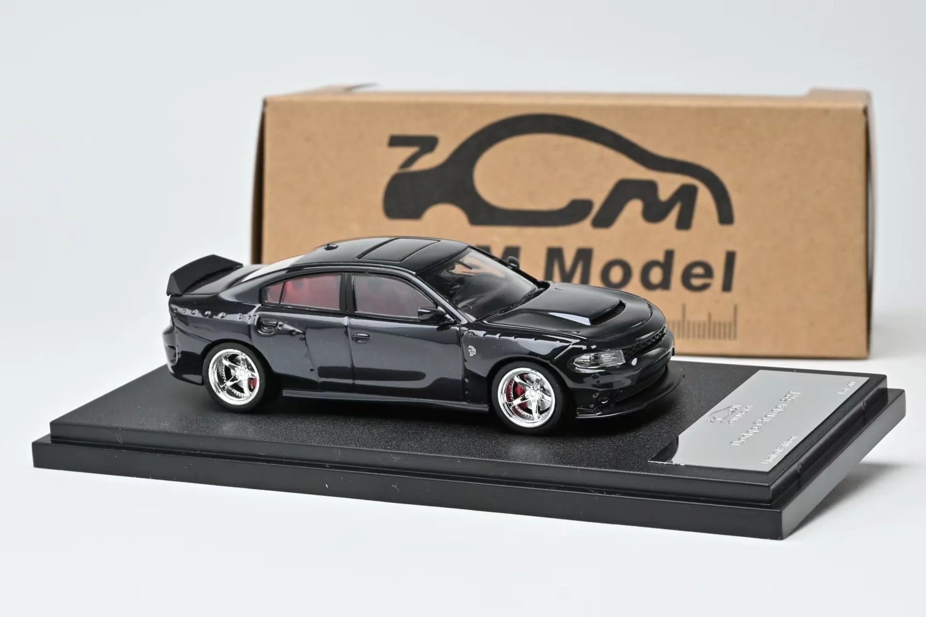 Black model car on a display stand with a branded box in the background
