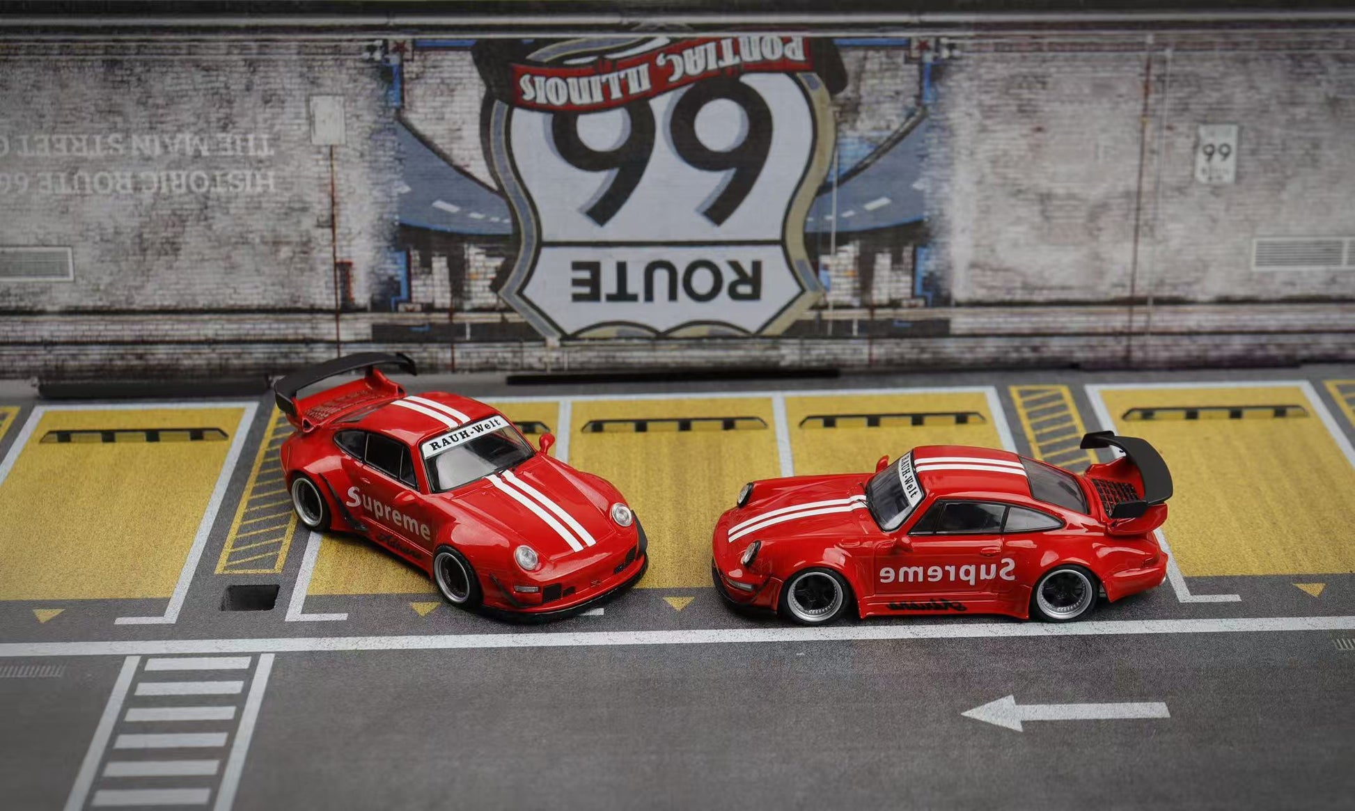 Two red model cars on a miniature road with Route 66 sign in the background