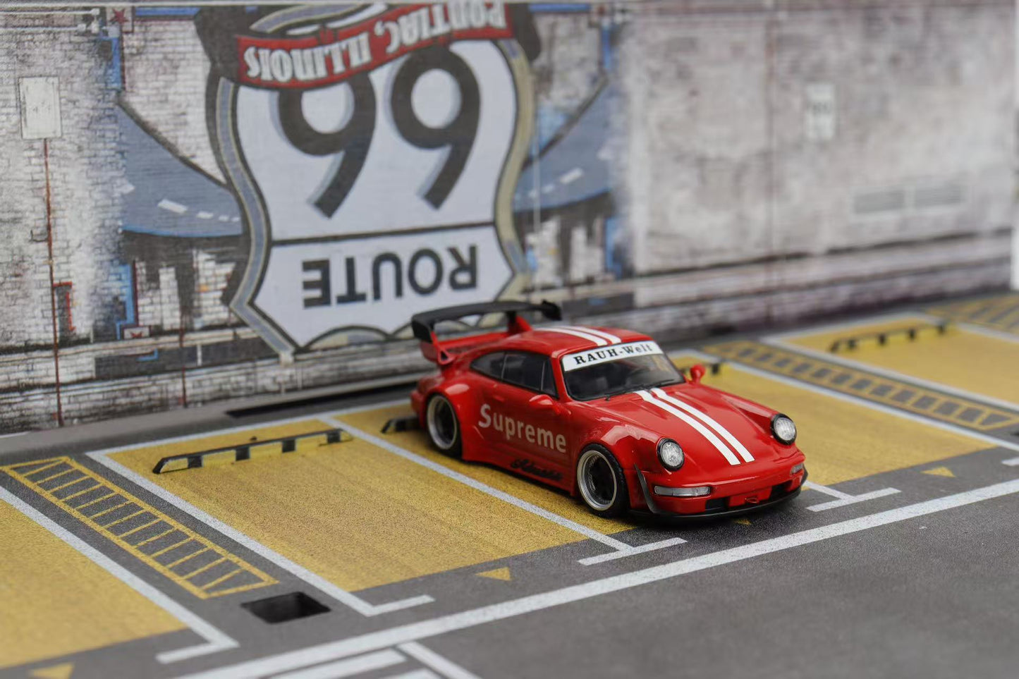 Red model car with 'Supreme' branding on a track with Route 66 sign in the background
