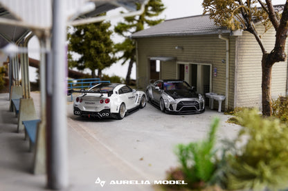 A miniature scale model diorama of two Nissan GT-R cars parked outside a small building, with the brand name 'Aurelia Model' visible at the bottom.