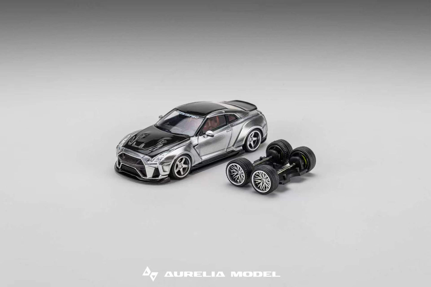 A miniature model of a silver and black sports car displayed next to its detached black wheels on a neutral gray gradient background. The brand name 'Aurelia Model' is visible at the bottom.