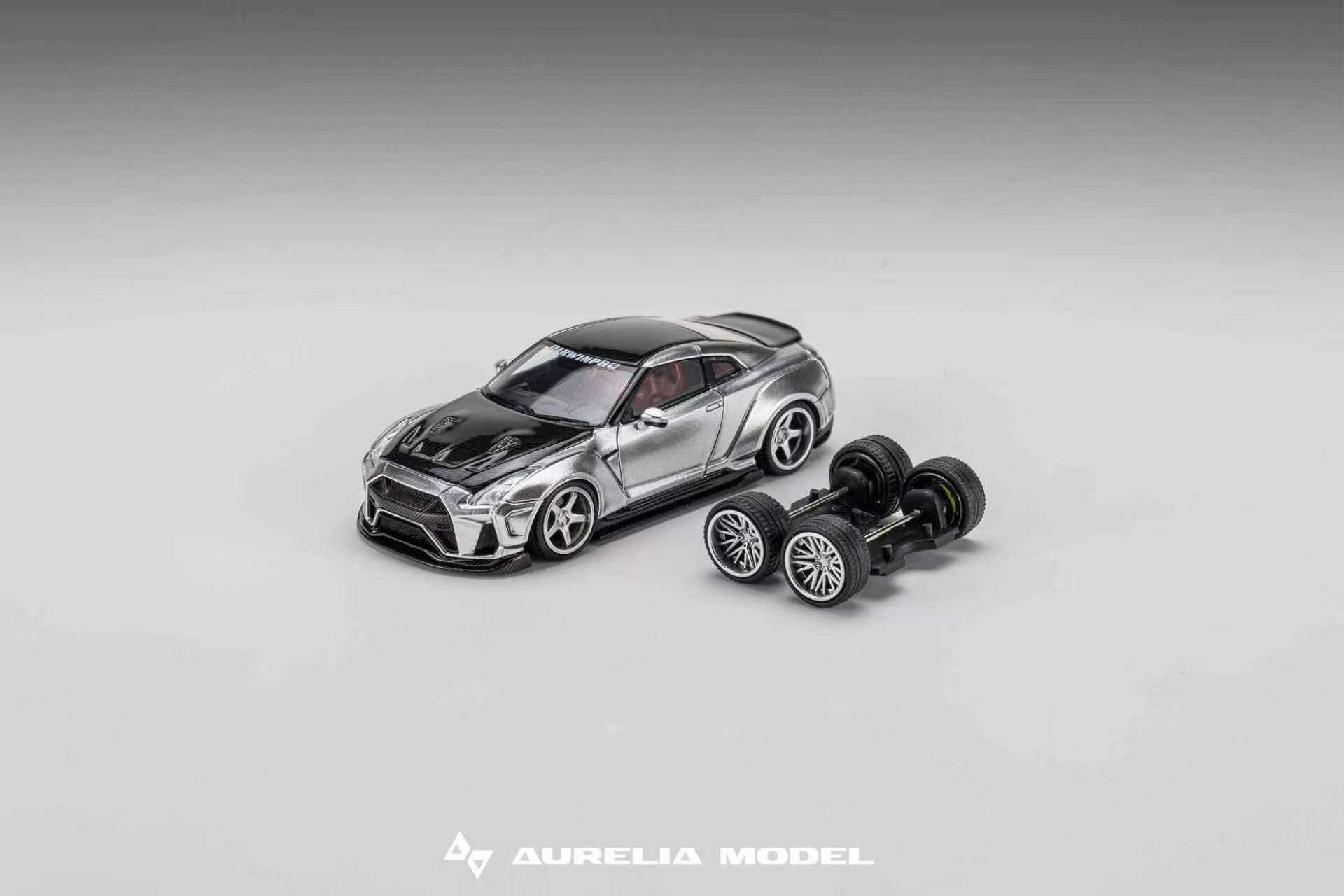 A miniature model of a silver and black sports car displayed next to its detached black wheels on a neutral gray gradient background. The brand name 'Aurelia Model' is visible at the bottom.